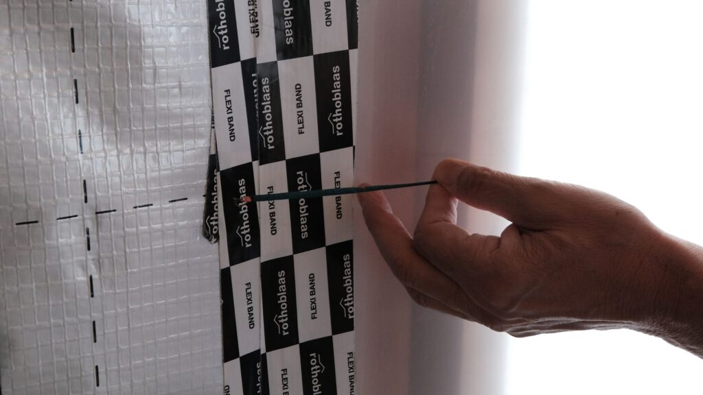 Mano che avvicina un filo di fumo a un giunto nastrato della barriera al vapore per individuare gli spifferi