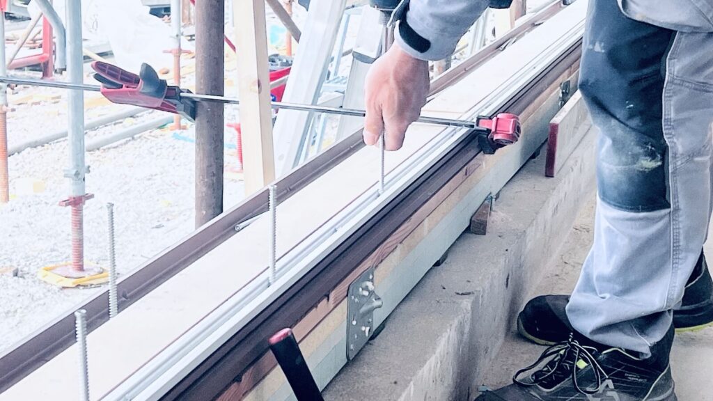 Operaio regola e mette a piombo la soglia di una grande porta scorrevole in cantiere.