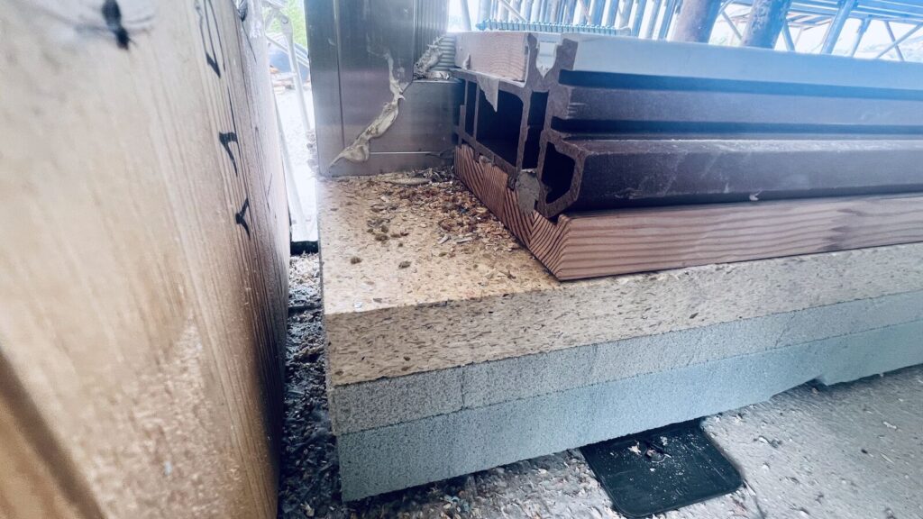 Stratigrafia della base d’appoggio di una porta scorrevole con strati di isolante e soglia in cantiere.