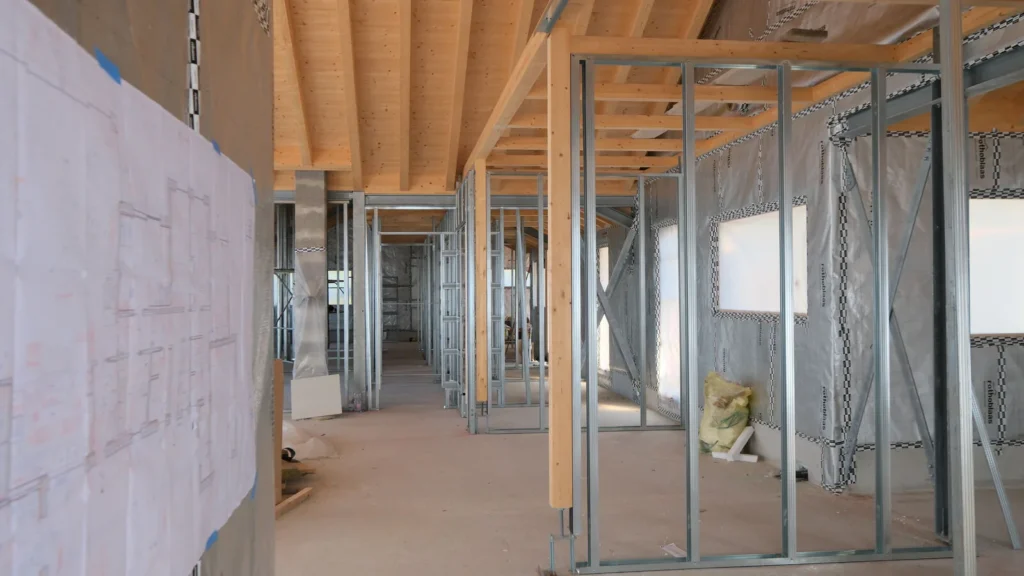 Disegno tecnico di dettaglio appeso a una parete di cantiere, con la struttura dei cartongessi sullo sfondo.