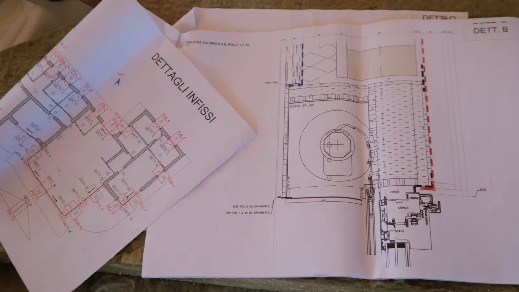 Disegni tecnici dei dettagli degli infissi aperti su un tavolo di cantiere.