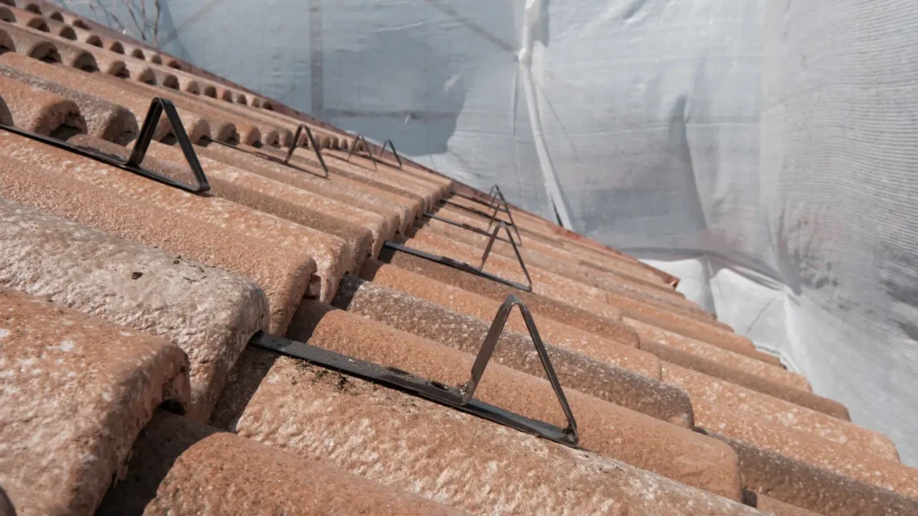 Fila di fermaneve metallici triangolari montati su tegole nuove, con teli bianchi di protezione sullo sfondo.