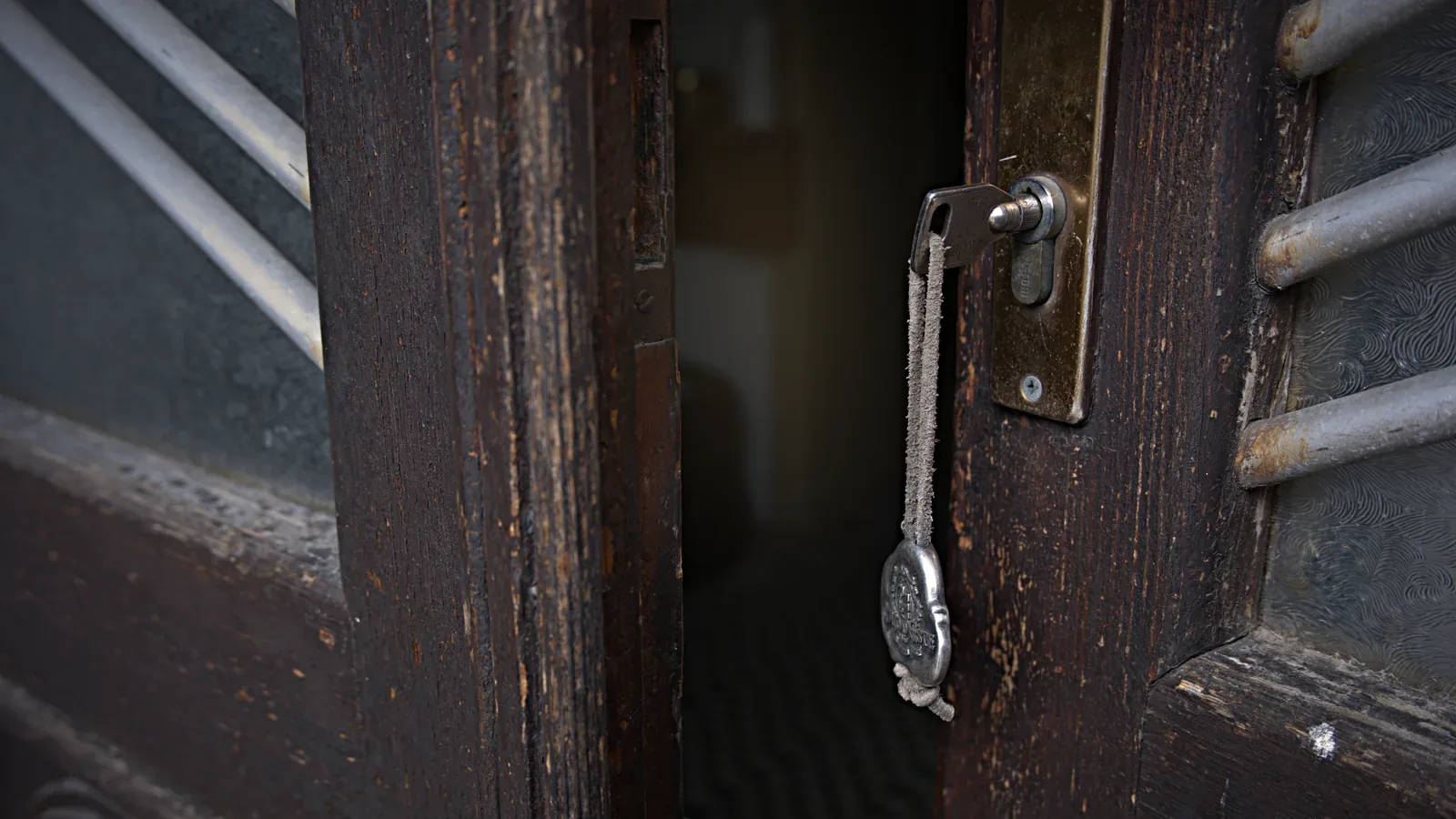 Chiave con medaglione inserita nella serratura di una vecchia porta in legno socchiusa.